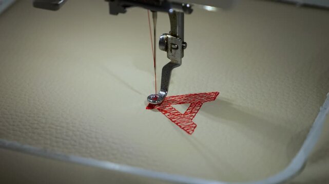 Machine embroidery of the letter "A" with red thread on light brown leather fabric.