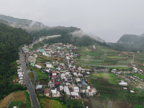 Aerial view of a hillside village with terraced fields and a winding road nestled among misty mountains in Tawangmangu, Central Java, Indonesia.