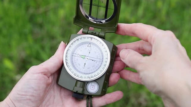 Compass in human hands against a background of green grass. Person navigates space using a compass. Concept of travel, adventure, and navigation.