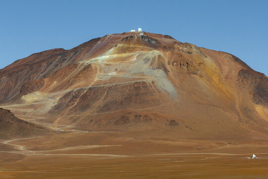 Aerial view of the Cerro Chajnantor Atacama Telescope situated on a high mountain peak amidst the arid desert landscape and winding roads in San Pedro de Atacama, Antofagasta, Chile.