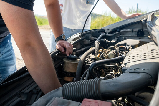 Person examining car engine under open hood due to vehicle breakdown on a road or highway, needing automotive repair