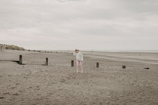 lone mature woman standing on vast empty beach under overcast sky