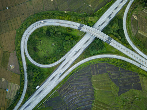 Aerial view of the Bawen - Salatiga toll roads interchange with curved ramps surrounded by lush green rice fields and agricultural land in Tengaran, Central Java, Indonesia.