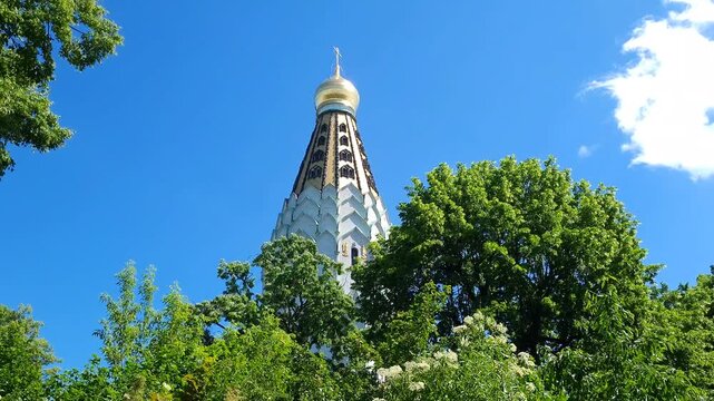 Golden dome of a christian orthodox church behind green trees on a bright sunny day