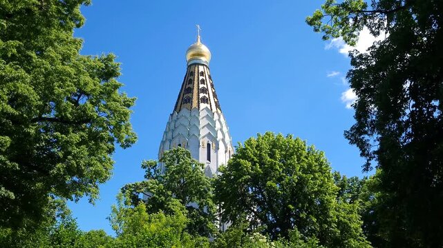 Golden dome of a christian orthodox church behind green trees on a bright sunny day
