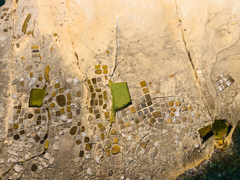 Aerial view of Xlendi Salt Pans carved into limestone rock with green algae and geometric patterns in Il-Munxar, Regjun Ghawdex, Malta.