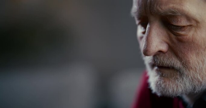 Thoughtful elderly bearded man in close-up side profile with dramatic lighting