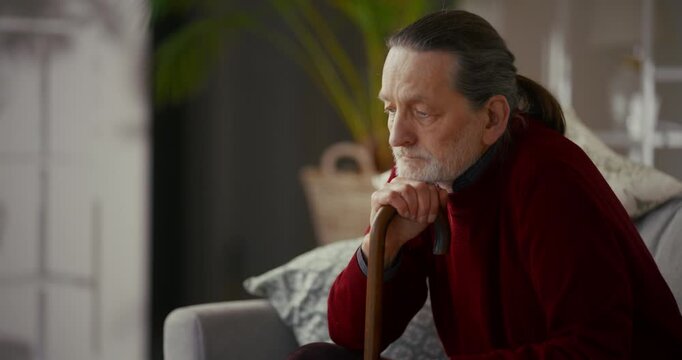 Elderly man with white beard sitting on sofa holding walking cane