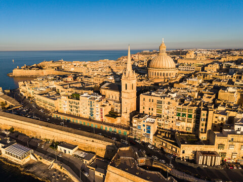 Aerial view of the Basilica of Our Lady of Mount Carmel and St Paul's Pro-Cathedral spire above the historic limestone buildings and fortifications of Valletta, Port Region, Malta.