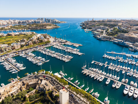Aerial view of the Msida Marina filled with luxury yachts and sailboats near historic fortifications under a clear blue sky in Ta' Xbiex, Eastern Region, Malta.