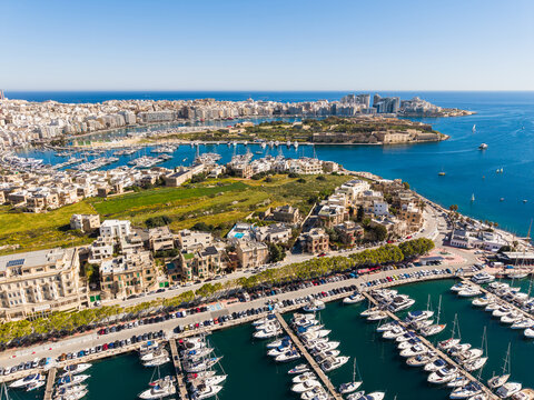 Aerial view of the Msida Marina and Ta' Xbiex waterfront with luxury yachts, historic buildings, and Manoel Island under a clear blue sky in Ta' Xbiex, Eastern Region, Malta.