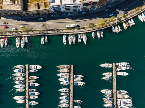 Aerial view of luxury yachts and sailboats moored at the marina docks along the turquoise waterfront with a coastal road and urban buildings Ta' Xbiex, Eastern Region, Malta.