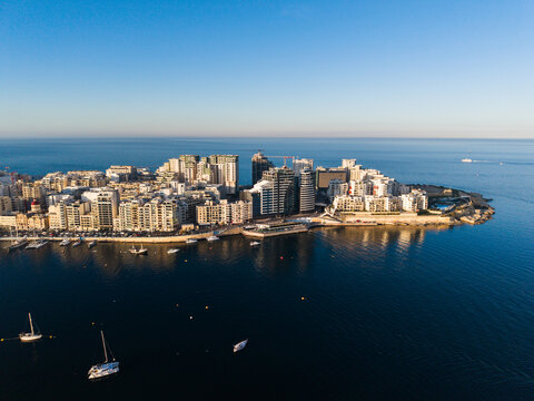 Aerial view of the modern waterfront buildings and harbor with sailboats under a clear blue sky in Sliema, Eastern Region, Malta.