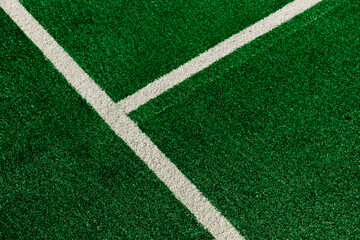 Close up view of white painted lines forming a boundary on a bright green artificial grass sports field. Stock background photo