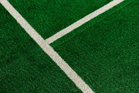 Close up view of white painted lines forming a boundary on a bright green artificial grass sports field. Stock background photo