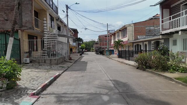 first person point of view walking down a quiet residential street lined with houses in a small colombian town