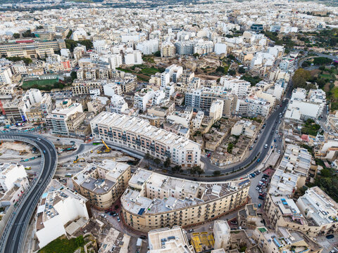 Aerial view of dense urban development with apartment buildings and curved road infrastructure in Msida, Eastern Region, Malta.