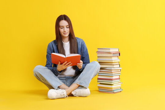 Young woman reading book and stack of colorful ones against yellow background