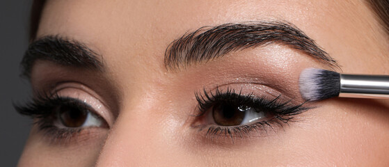 Naklejka premium Applying eye shadow with brush onto woman's face against grey background, closeup
