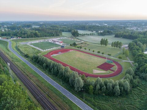 Diepenbeek, Belgium. Aerial drone view of athletics track and football fields near railway and road in green rural landscape at sunrise