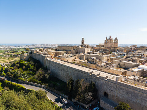 Aerial view of the historic fortified city of Mdina with its massive stone bastions, St. Paul's Cathedral, and limestone architecture under a clear blue sky in Mdina, Western Region, Malta.