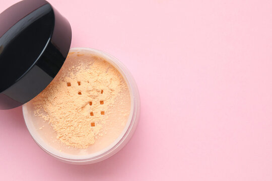 Loose face powder and lid on pink background, top view. Space for text