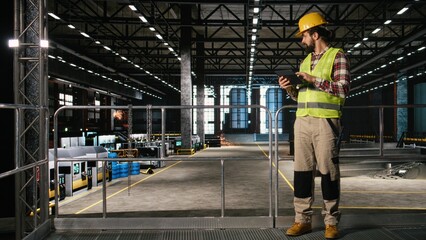 Man engineer wearing helmet and checking production line on tablet, walking through industrial space filled with massive machinery, Warehouse environment showcases heavy industry worksite. © DC Studio