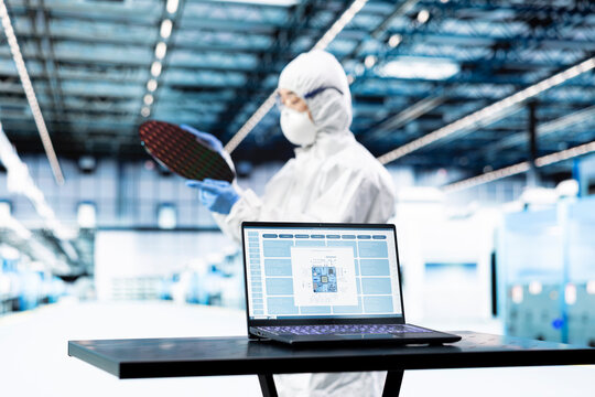 Microchip factory specialist testing silicon wafer batches with laptop EDA software, Hardware designer monitoring semiconductor manufacturing plant machinery readouts with notebook program.