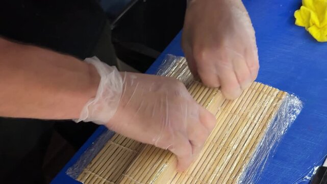 Skilled chef carefully cuts sushi rolls into even pieces using a sharp knife while preparing fresh japanese cuisine on a blue workstation