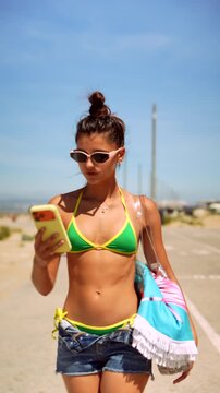 Young woman walking along a sunny coastal road with beach gear