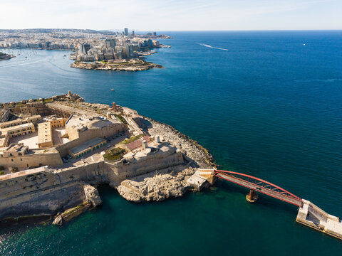 Aerial view of Abercrombie's Bastion and the red St Elmo Bridge spanning the deep blue sea along the historic coastal fortifications of Valletta, Port Region, Malta.