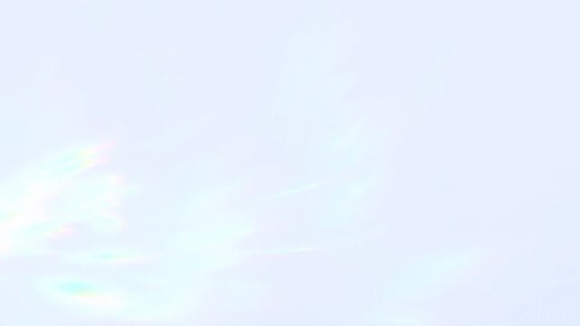 Slow motion panning shot of iridescent cloud streaks drifting across pale daytime sky in wide minimal composition