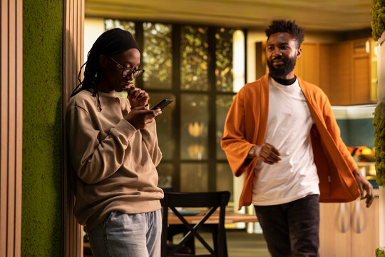 Black boyfriend seeing her girlfriend laugh at mobile phone screen, being suspicious about a potential affair, worrying about infidelity and dishonesty, Controlling toxic man in rage, bullying.