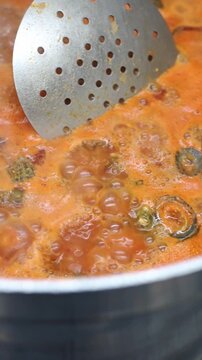 Fresh limpets boiling in a savory tomato sauce inside a large metal pot. A professional chef is stirring the delicious seafood dish