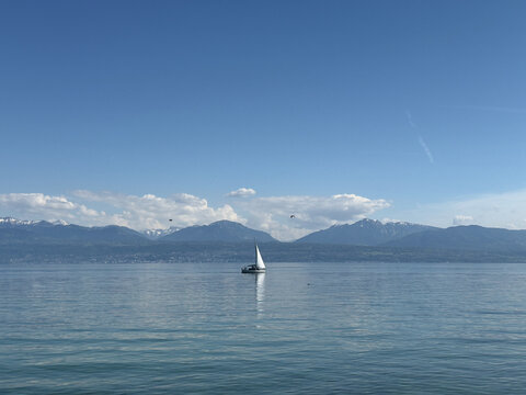 Single Sailing Boat on the Calm Turquoise Waters of a Scenic Swiss Lake With Alpine Mountains Beyond