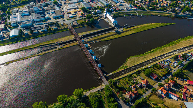Aerial view of the Vltava river with a weir and a bridge crossing the water near industrial and residential areas in Veltrusy, Central Bohemian Region, Czechia.