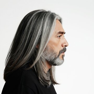 Man profile studio shot. Long layered grey hair and goatee beard. Male adult with stylish haircut and facial hair. Clean white background portrait.