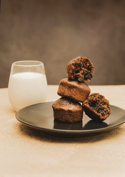 Stack of chocolate muffins with one open on a black plate on a black and gold background with a glass of milk.