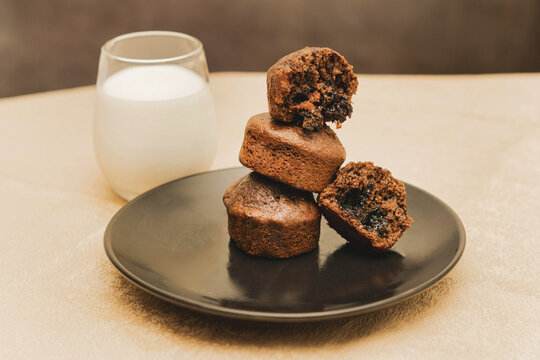 Stack of chocolate muffins with one open on a black plate on a black and gold background with a glass of milk.