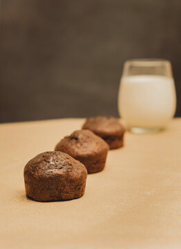 Stack of chocolate muffins on a gold mat and black background with a glass of milk