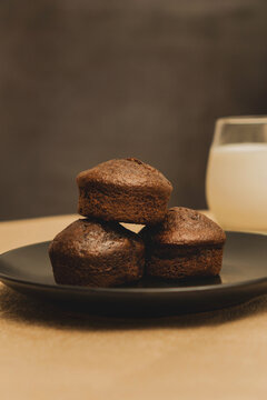 Stack of chocolate muffins on a black plate on a gold metal and black background with a glass of milk