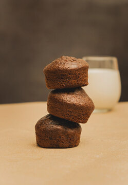 Stack of chocolate muffins on a gold mat and black background with a glass of milk
