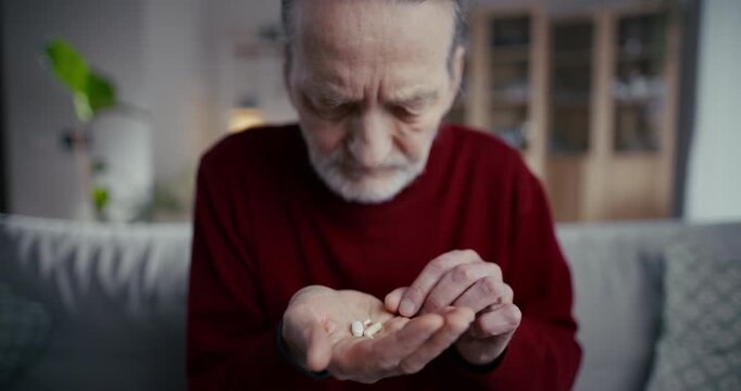 Elderly man sitting on a sofa and examining his hand in a living room