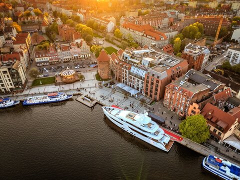 Aerial view of a large white yacht moored along the Motlawa River waterfront with historic brick buildings and a carousel in Gdansk, Pomeranian Voivodeship, Poland.