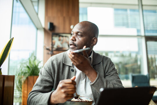 Mature man using voice assistant at cafe workspace during breakfast