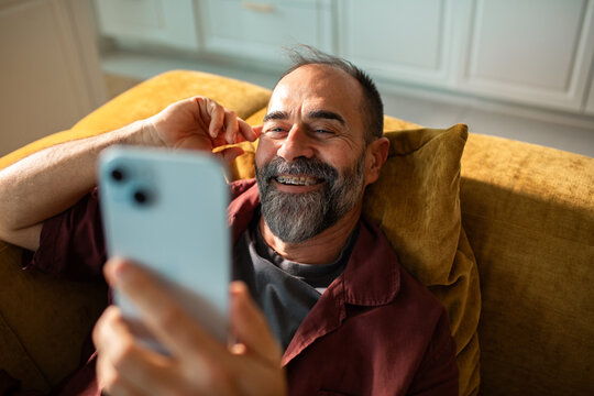 Smiling middle-aged man video chatting on smartphone at home