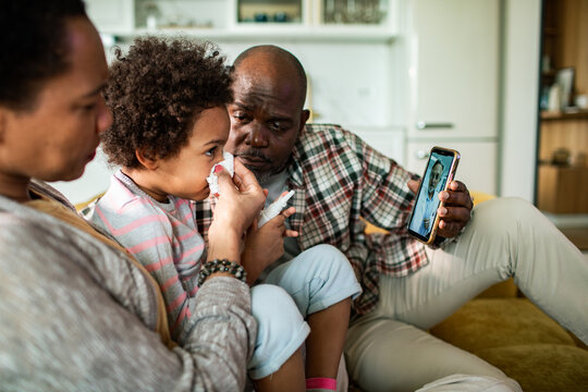 Parents comforting sick child during telehealth video call at home