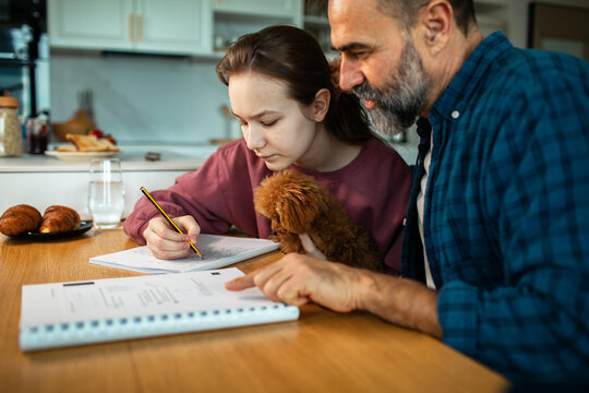 Father helping teen daughter with homework at kitchen table