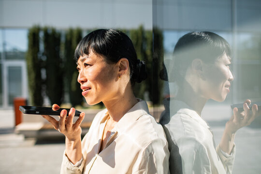 Businesswoman using voice assistant on smartphone outside office