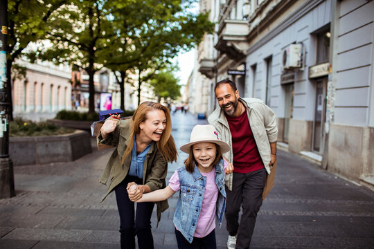 Happy family with daughter running on city shopping street